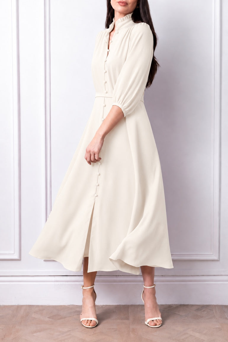 Front three-quarter view of the Aurelia ivory dress, with frill collar, covered buttons, matching belt and flared skirt.